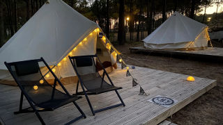 Bell Tent Tipi-Zelte mit Lichterketten und Stühlen auf Holzplattform, idyllisch im Wald bei Dämmerung.
