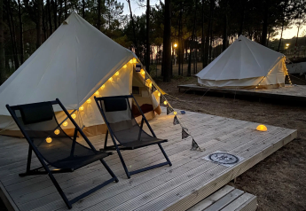 Tentes tipi Bell Tent avec guirlandes lumineuses et chaises sur terrasse en bois dans une forêt au crépuscule.