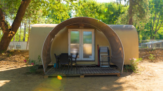 Tenda safari chiamata Coco Suite Lake con veranda, sedie e tavolo, immersa tra alberi e natura.