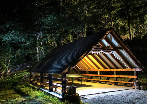 Illuminated wooden shelter at Bedura Park Campsite in Catalonia, Spain, surrounded by forest at night.