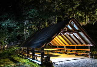 Illuminated wooden shelter at Bedura Park Campsite in Catalonia, Spain, surrounded by forest at night.