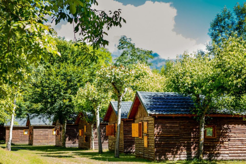 Wooden cabins amongst green trees at Campsite Bedura Park, a holiday park in Catalonia, Spain under blue sky.