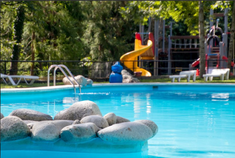 Outdoor swimming pool with rocks in front and playground in the background at Bedura Park, Catalonia, Spain.