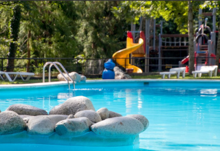 Outdoor swimming pool with rocks in front and playground in the background at Bedura Park, Catalonia, Spain.