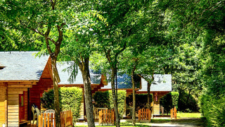 Bungalow Comfort casette in legno immerse nel verde, giorno soleggiato con verande e sedie all’esterno.