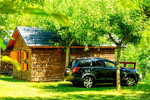 Black car parked by Bungalow “Zen” at Campsite Bedura Park, Spain, surrounded by lush green trees.