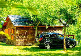 Black car parked by Bungalow “Zen” at Campsite Bedura Park, Spain, surrounded by lush green trees.