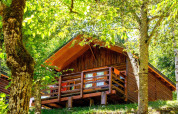 Comfort Bungalow in hout op Bedura Park camping in Spanje, omringd door frisse bomen en zomerzon.