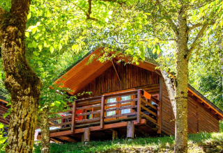 Wooden Comfort Bungalow at Campsite Bedura Park in Spain, surrounded by lush green trees and sunlight.