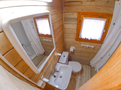 Kleine badkamer met houten muren, raam met gordijn, toilet, lavabo en spiegel in Bungalow Comfort.