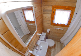 Kleine badkamer met houten muren, raam met gordijn, toilet, lavabo en spiegel in Bungalow Comfort.