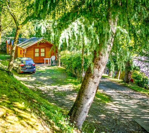 Cabaña de madera en Bungalow Comfort, en el Camping Bedura Park, España, rodeada de árboles y coche.