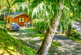Bungalow in legno al Camping Bedura Park in Spagna, circondato da alberi con auto parcheggiata davanti.