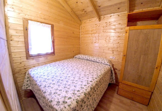 Wood-paneled bedroom in Bungalow Zen at Campsite Bedura Park, Spain, featuring a double bed and wardrobe.
