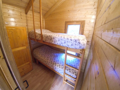 Habitación estrecha de cabaña con literas de madera, ropa de cama floral y una ventana pequeña.