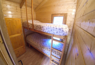 Narrow cabin bedroom with wooden bunk beds, floral bedding, and a small window letting in natural light.