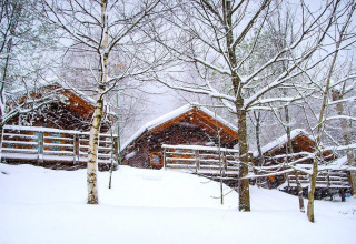 Cozy wooden cabins in heavy snowfall at Bedura Park campsite in Spain, surrounded by snow-covered trees.