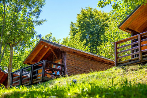 Bungalow Zen wooden cabin with a porch, nestled among lush green trees on a sunny hillside.