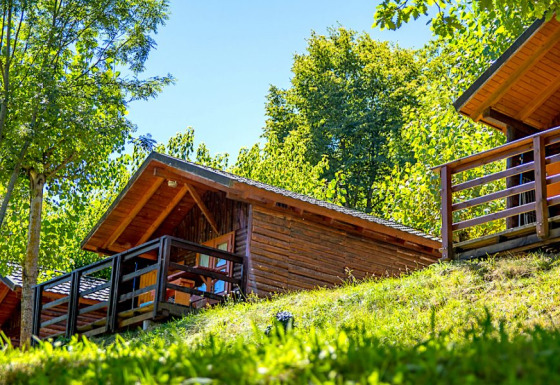 Cabaña Bungalow Zen de madera con terraza, rodeada de árboles verdes en una ladera soleada.