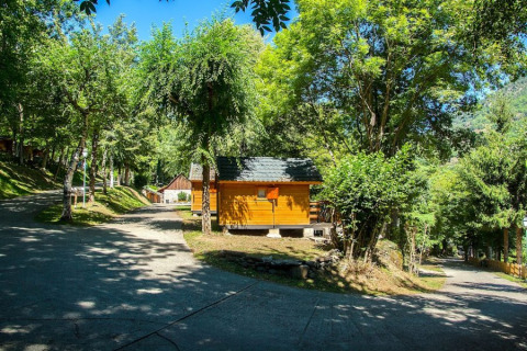 Holzhütten im Campsite Bedura Park in Spanien, umgeben von grünen Bäumen und sonnigem Himmel.