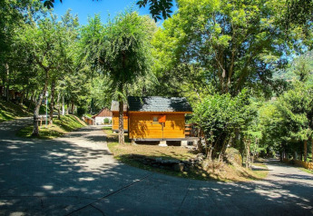 Cabaña de madera entre árboles verdes y luz solar en el Camping Bedura Park, España, en un día tranquilo.