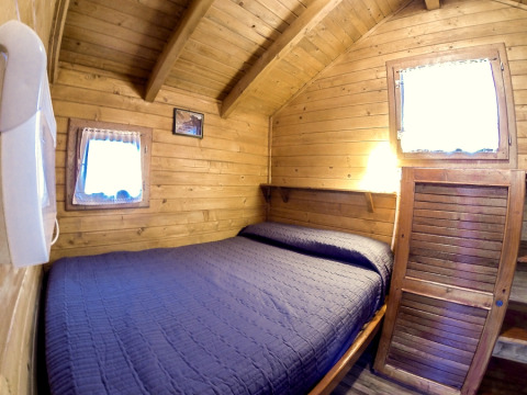 Cozy wooden cabin with a double bed, blue quilt, and two small windows at Campsite Bedura Park, Spain.