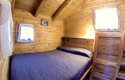 Accogliente baita in legno con letto matrimoniale, copriletto blu e due finestre al Bedura Park, Spagna.