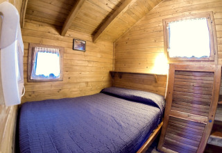 Accogliente baita in legno con letto matrimoniale, copriletto blu e due finestre al Bedura Park, Spagna.
