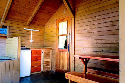 Interior de una acogedora cabaña de madera en el Camping Bedura Park, España, con cocina y banco.