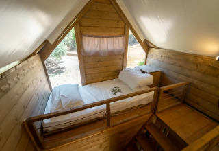Indvendigt billede af en hyggelig træseng på hems i et safari-telt ved Vallicella Glamping Resort, Italien.