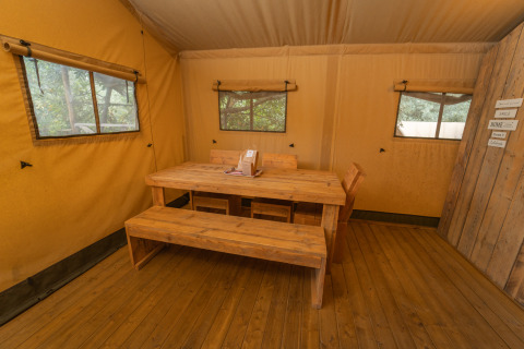 Intérieur du Safari Lodge 1 au Vallicella Glamping Resort en Italie, avec table et bancs en bois.
