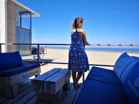 Mujer con vestido azul en terraza con vistas a la playa en Zonneweelde Lodge Deluxe, Camping Zonneweelde.