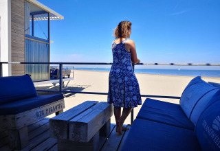 Mujer con vestido azul en terraza con vistas a la playa en Zonneweelde Lodge Deluxe, Camping Zonneweelde.