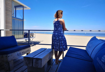 Femme en robe bleue sur une terrasse avec vue sur la plage à Zonneweelde Lodge Deluxe, Camping Zonneweelde.