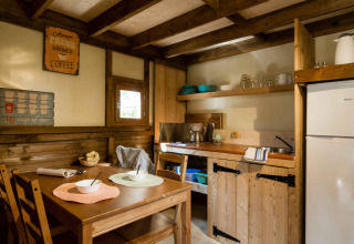 Coin cuisine dans la tente safari Air Dreamer 3, décor bois, table à manger et étagères ouvertes avec vaisselle.