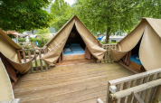 Tente safari avec terrasse en bois et trois espaces de couchage, entourée d’arbres verts luxuriants.