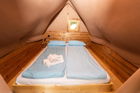 Espace nuit dans une tente safari avec deux lits simples, draps bleus et murs en bois.
