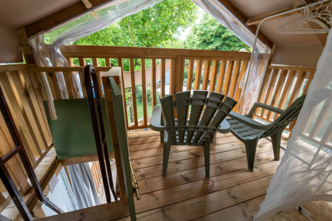 Balkon bij Air Lodge glamping met twee plastic stoelen, houten leuning en zicht op groene buitenbomen.