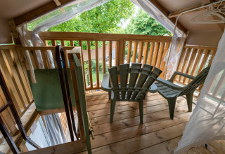 Balkon bij Air Lodge glamping met twee plastic stoelen, houten leuning en zicht op groene buitenbomen.