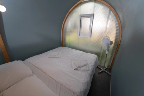 Et glampingværelse i Coco Couple med dobbeltseng, hvidt sengetøj, lille vindue og en ventilator.