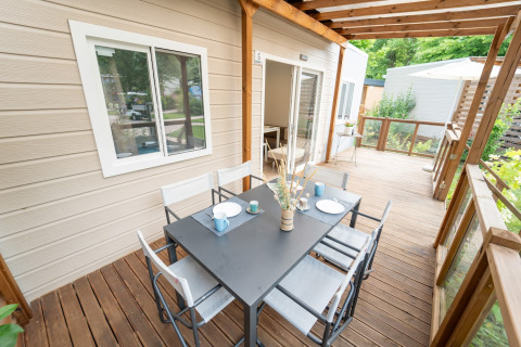 Terrasse en bois d’un hébergement glamping avec table à manger noire, six chaises et vue verdoyante.