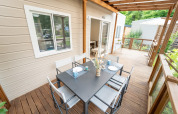 Terrasse en bois d’un hébergement glamping avec table à manger noire, six chaises et vue verdoyante.