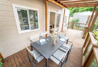 Terrasse en bois d’un hébergement glamping avec table à manger noire, six chaises et vue verdoyante.