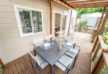 Terrasse en bois d’un hébergement glamping avec table à manger noire, six chaises et vue verdoyante.