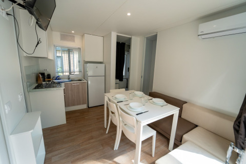 Hébergement glamping moderne avec kitchenette, table à manger, canapé, climatisation et télévision.