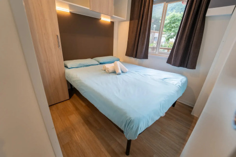 Chambre avec lit double, draps bleu clair et fenêtre dans Cottage Next XL supérieur, Vallicella Glamping Resort en Italie.