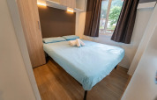 Chambre avec lit double, draps bleu clair et fenêtre dans Cottage Next XL supérieur, Vallicella Glamping Resort en Italie.