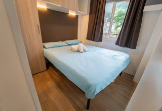 Chambre avec lit double, draps bleu clair et fenêtre dans Cottage Next XL supérieur, Vallicella Glamping Resort en Italie.