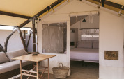 Interno di una tenda safari con pavimento in legno, divano, tavolo, cestino e letto matrimoniale.