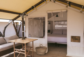 Interno di una tenda safari con pavimento in legno, divano, tavolo, cestino e letto matrimoniale.